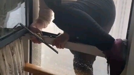Nhân viên vệ sinh đứng ngoài bệ cửa sổ lau kính mà không có bất kỳ biện pháp bảo hộ nào