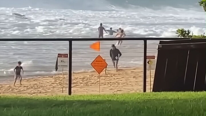 Surfer on a beach vacation: spots a woman swept away by the waves and rushes in to rescue her from d
