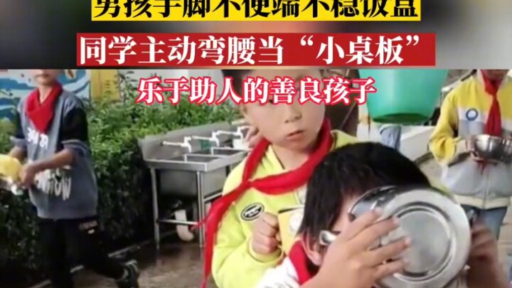 เด็กชายเคลื่อนไหวมือและเท้าลำบาก จึงถือกล่องข้าวไม่ค่อยอยู่ เพื่อนร่วมชั้นจึงย่อตัวลงทำหน้าที่เป็น “