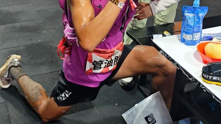 Guan Yousheng creates another iconic moment at the aid station: stretching while eating noodles.