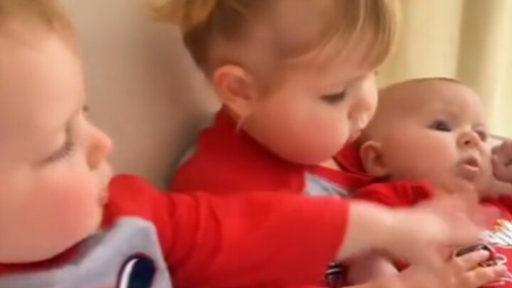 Two adorable kids get into a squabble over who gets to hold the baby...