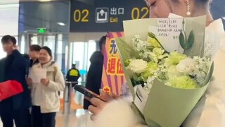 女生站在车站穿着漂亮的衣服，手捧鲜花去接她的男孩回家