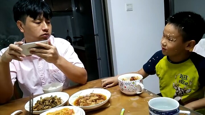 Dad keeps playing on his phone instead of eating, so the son slams the table in anger and shouts, "H