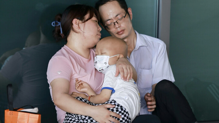 A bald-headed child and their family of three are resting in a cool corner of the hospital. I don’t 