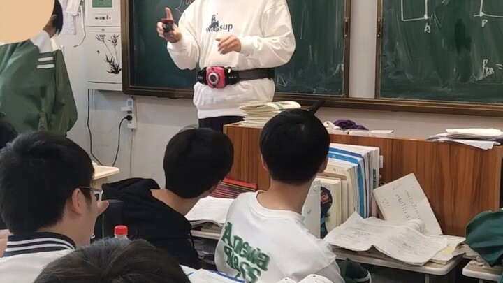 Ajari teman sekelas untuk memakai sabuk Kamen Rider dan berubah menjadi pekerja sosial di podium.