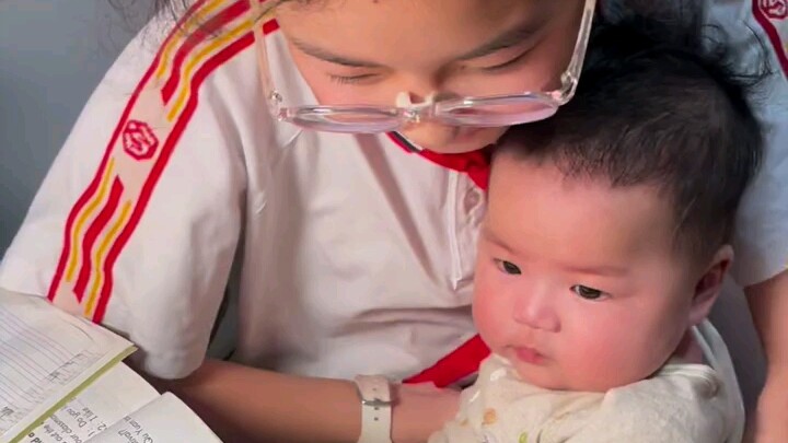 พี่สาวกำลังเขียนหนังสือ ส่วนน้องชายกอดอยู่ในอ้อมแขนไม่ยอมไปไหน 😁