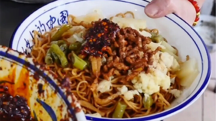 Mì luộc nóng hổi chan nước dùng thịt, thêm thịt sợi và rau củ, rưới chút ớt dầu cùng trứng chiên, lạ