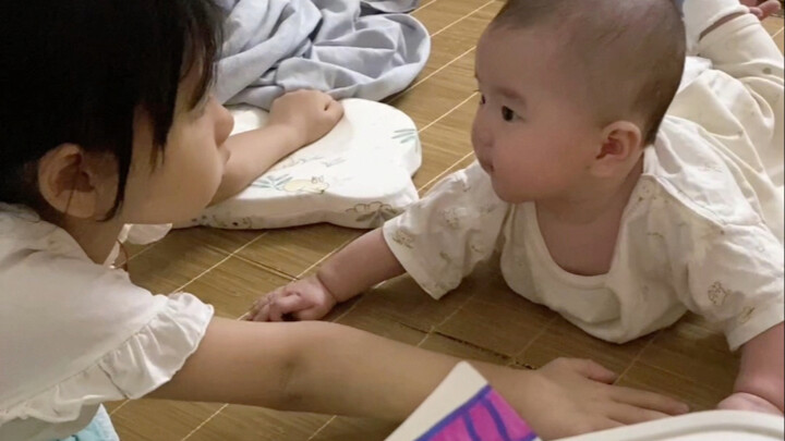 A 5-year-old sister imitates the actions of a 4-month-old baby, leaving the baby completely confused