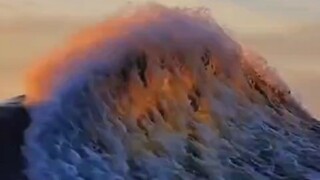 The sunlight of the sunset shines through the waves.