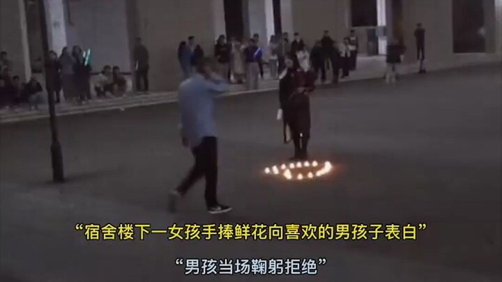 “ที่หน้าหอพัก สาวน้อยถือช่อดอกไม้มาสารภาพรักกับหนุ่มที่ชอบ ผู้คนยืนมุงดูเต็มไปหมด แต่หนุ่มกลับโค้งคำ