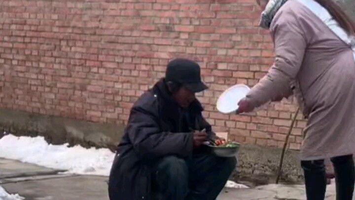 Para sesepuh desa duduk bersila di depan tikar, sementara seorang perempuan yang sedang mencuci piri