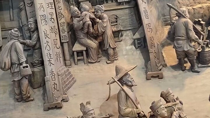 ตัวละคร ดอกไม้ ต้นไม้ในภาพถูกแกะสลักเป็นรูปสามมิติอย่างสมจริง งานไม้แกะสลัก “ภาพวาดแม่น้ำชิงหมิง” แบ